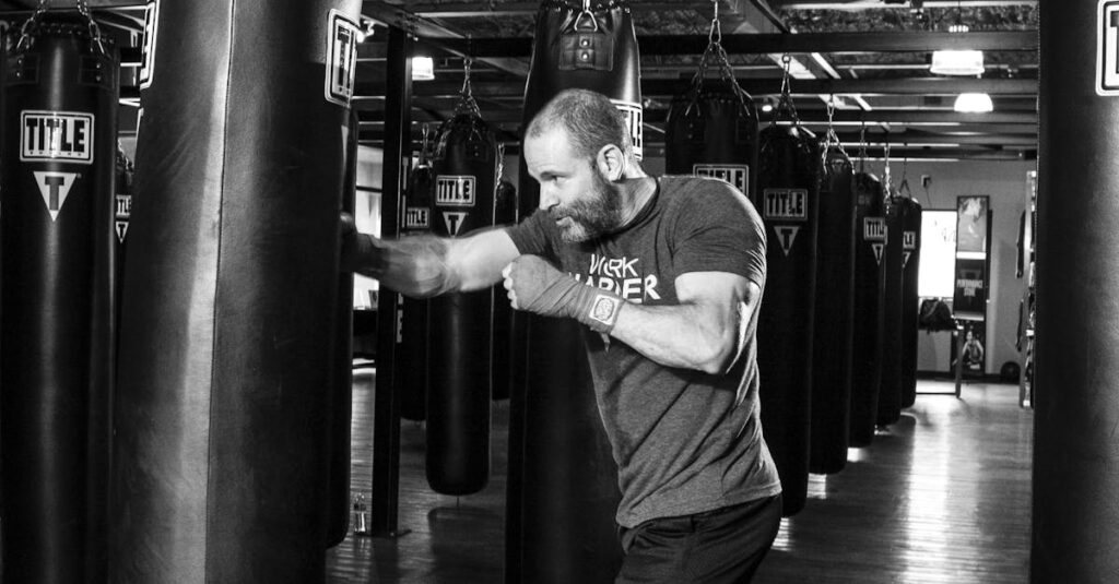 A man boxing with a punching bag in a gym, captured in black and white.